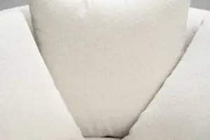 תקריב של ריפוד CLAM בז, בעל מרקם על כיסא או כרית, עם דוגמה גיאומטרית עם משולשים הנפגשים במרכז. הבד נראה רך וקטיפה, המעיד על משטח ישיבה נוח.