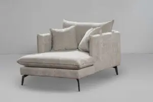 ARM CHAIR SAND הוא כסא נוח בקטיפה באפור בהיר המגיע עם שתי כריות גדולות ושתי כריות קטנות. הוא כולל רגליים שחורות חלקות על רקע אפור רגיל, המציג עיצוב מודרני ומינימליסטי.