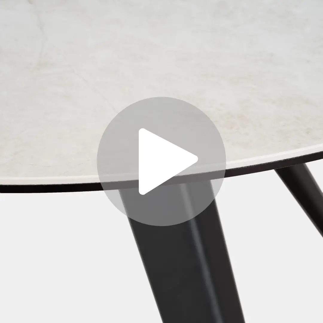 שולחן האוכל העגול LOKO, הכולל פלטה בהירה ורגליים שחורות בזווית, נראה חלקית. שכבת-על של לחצן הפעלה מזמינה את הצופים להעמיק בפינת אוכל עגולה האלגנטית הזו.