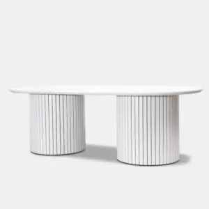 MARMOR WHITE שולחן סלון לבן מתהדר בחלק העליון אובלי המוחזק על ידי שני בסיסים גליליים המעוטרים בקווים שחורים אנכיים, היוצרים ניגודיות בולטת על רקע אפור בהיר רגיל.