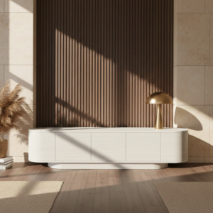 פנים מודרני כולל מזנון טלוויזיה מינימליסטי בצבע לבן של FOX עם מנורה זהובה מעליו, על רקע קיר כהה עם דוגמת לוחות עץ. אור השמש מדגיש את רצפת העץ והקירות בצבע בז', בעוד קישוט מעשב פמפס מדגיש את הצד השמאלי.