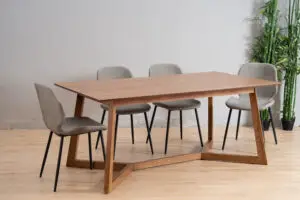 שולחן אוכל מודרני מעץ עם רגליים זוויתיות מוקף בחמש כיסאות מרופדים באפור עם רגליים ממתכת שחורה — רהיטים איכותיים המעניקים לחדר מראה יוקרתי. הסט מונח על רצפת עץ בהירה, עם צמחים ירוקים לצד השולחן על רקע קיר אפור חלק.