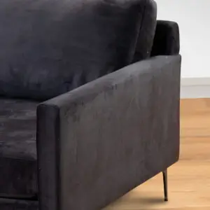 תקריב של משענת היד הימנית והכרית של כורסת ARM CHAIR MAMBA מבד קטיפה אפור כהה עם רגליים שחורות ודקות, המוצבת על רצפת עץ בהירה מול קיר לבן.