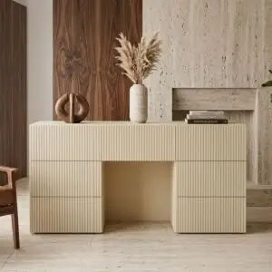 שולחן קונסולה מודרני בצבע בז' עם חריצים אנכיים, המוצע במחיר מוזל (מלאי מוגבל), ניצב מול אח מאבן מרקמת. על השולחן מונחים אגרטל קרמיקה עם עשב פמפס, ערימת ספרים ופסל עגול מופשט. קירות החדר מחופים בלוחות עץ.